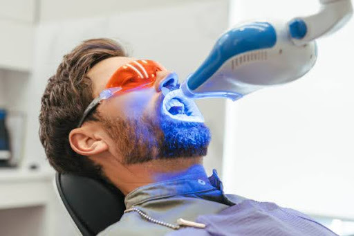 Dentist performing teeth whitening procedure on male patient