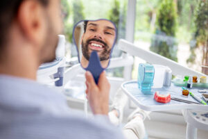 Happy Young Man Holding Mirror Admiring Smile After Dental Treatment